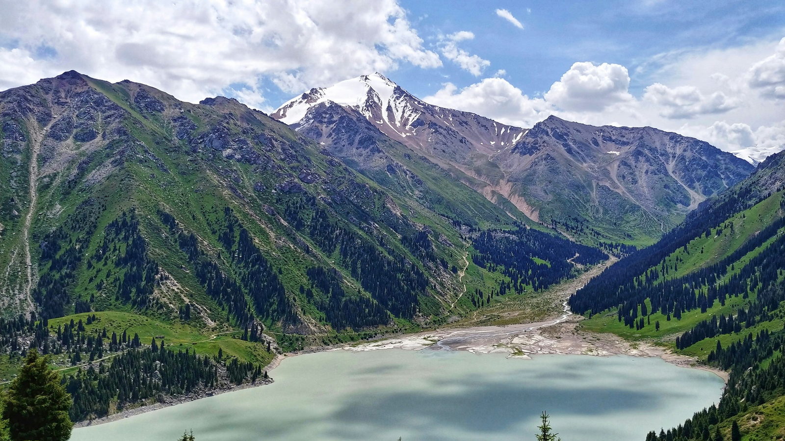 The turquoise water of Big Almaty Lake surrounded by forested mountains