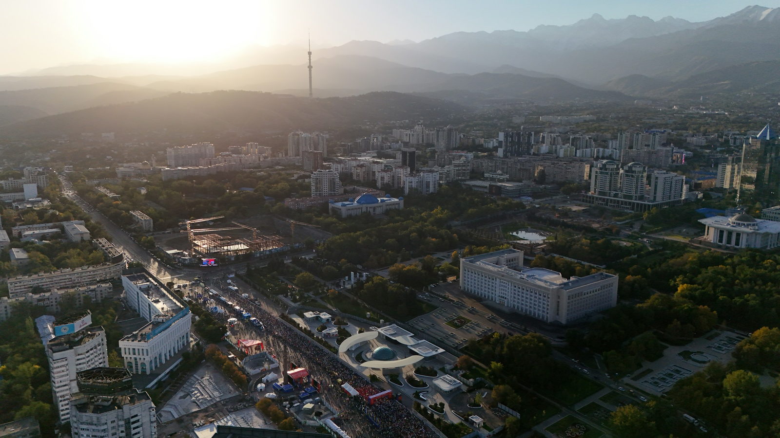 Aerial view of Almaty at sunset, wide tree-lined avenues running towards the mountains