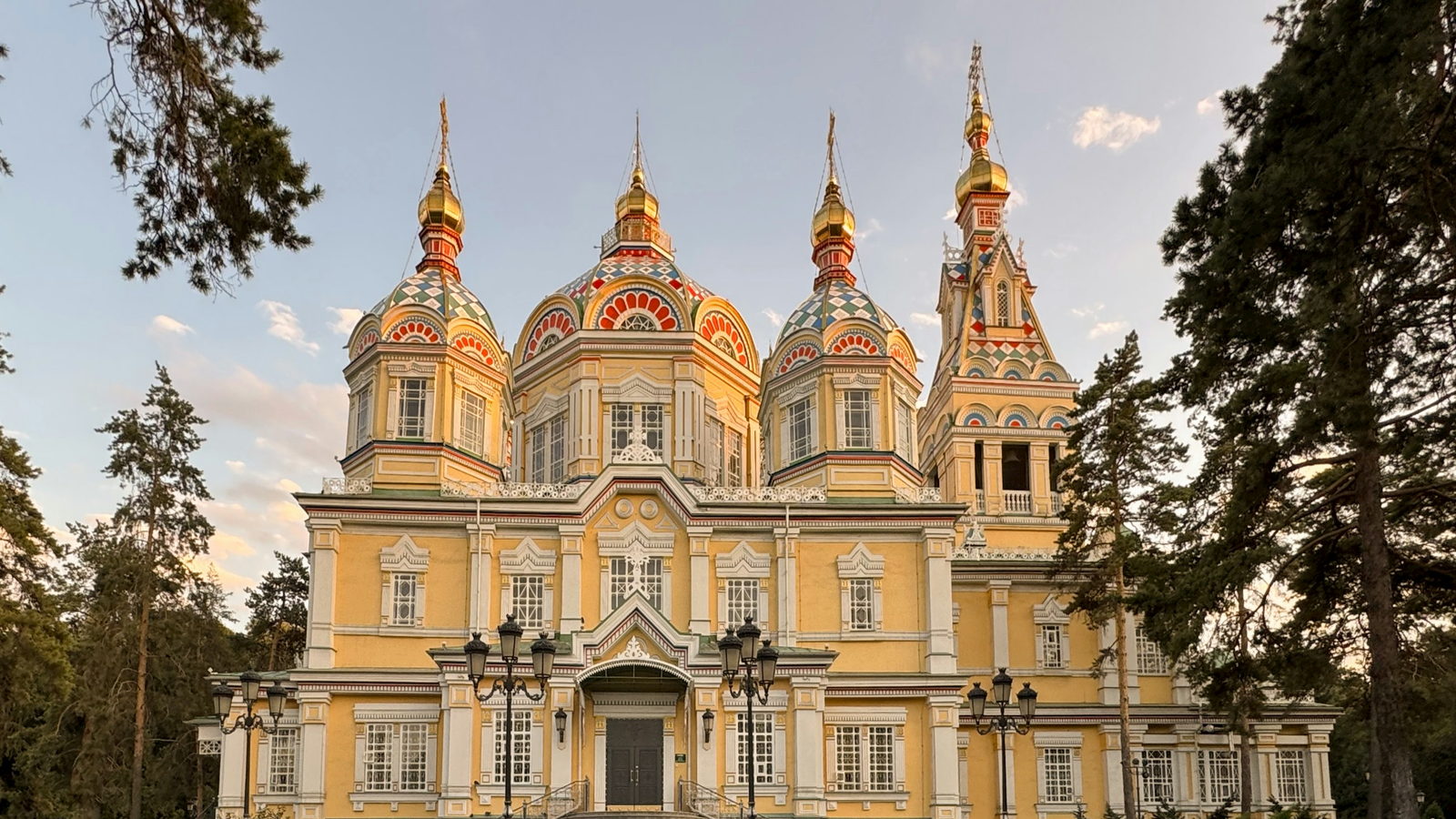 The yellow timber Ascension Cathedral and its coloured onion domes, framed by conifers in Panfilov Park
